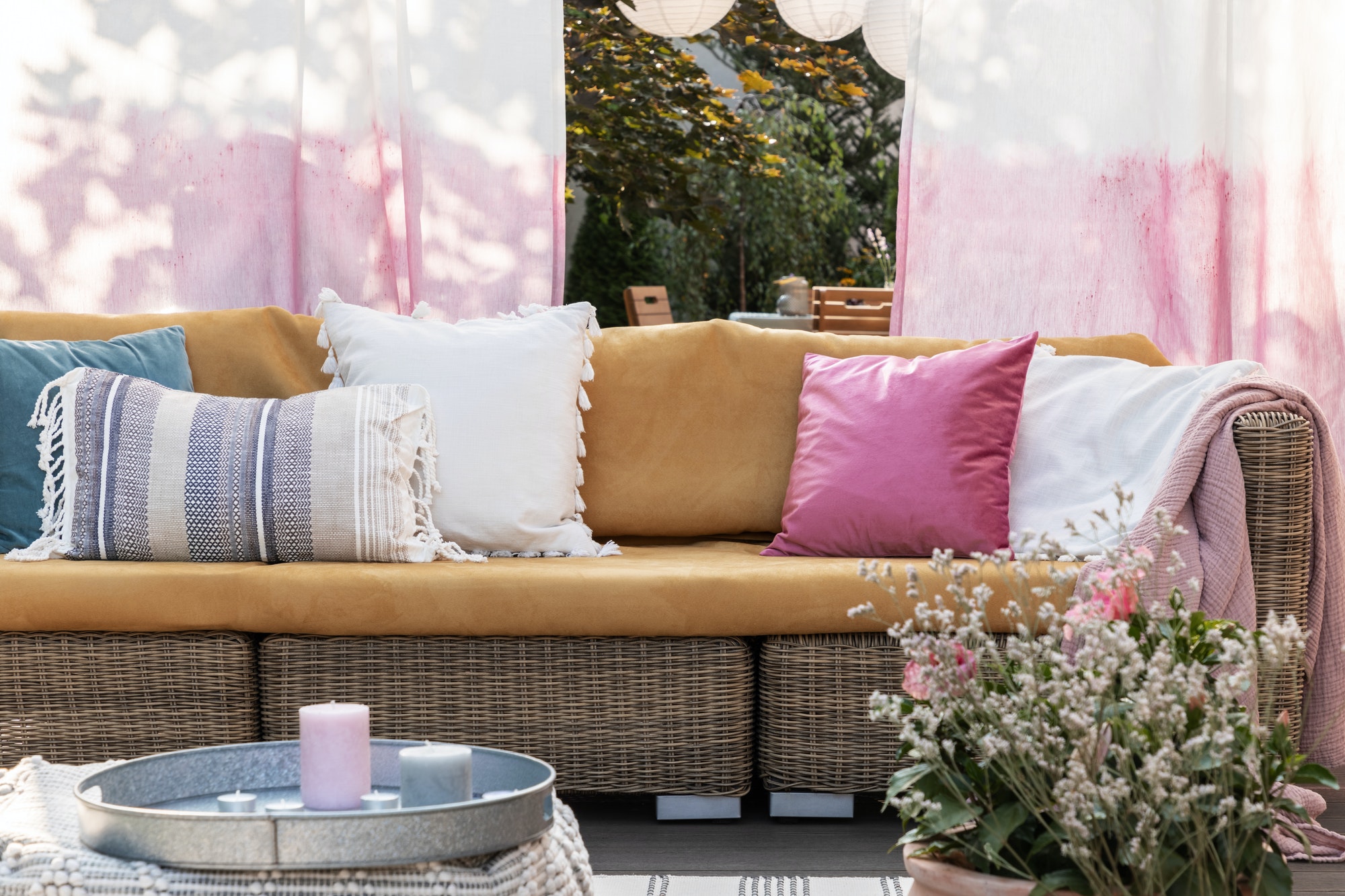 Colorful pillows on rattan sofa in the conservatory with flowers, painted drapes and candles. Real photo