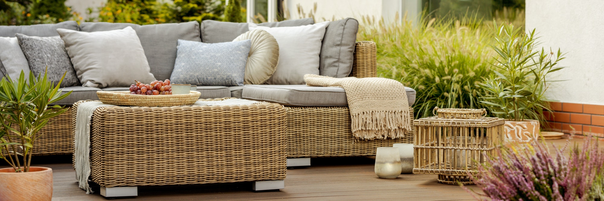 Comfortable wicker garden furniture with grey pillows in beautiful backyard