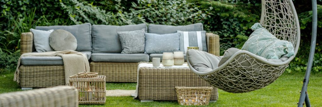 Comfortable wicker garden furniture with grey pillows in beautiful backyard