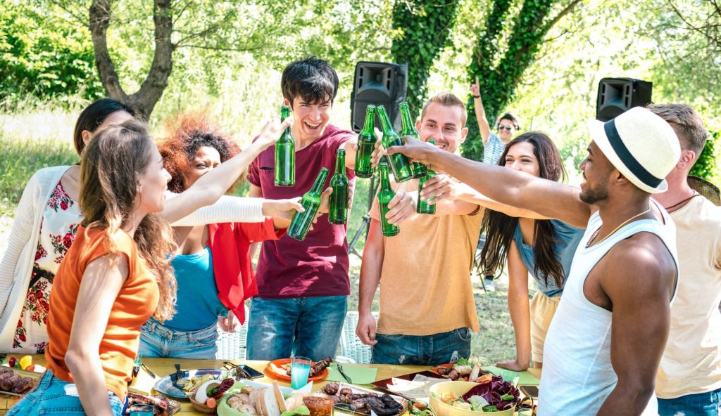 Happy multiracial friends toasting beer at barbecue garden party